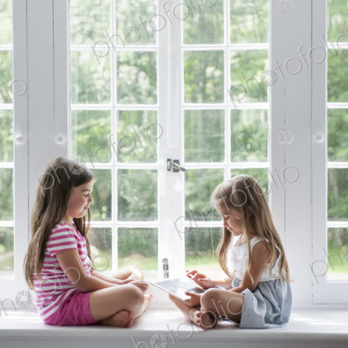 Two girls playing, sharing a digital tablet.