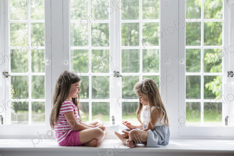 Two girls playing, sharing a digital tablet.