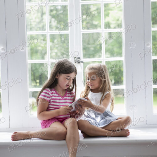 Two girls playing, sharing a digital tablet. Two girls playing, sharing a digital tablet.