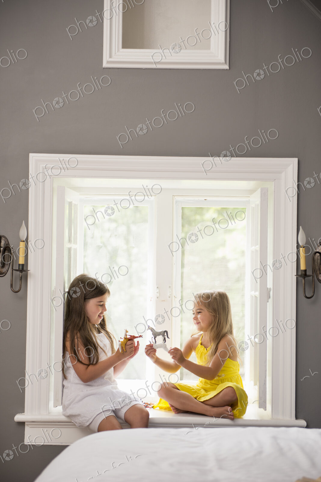 Two girls playing together, sitting on a window seat indoors.
