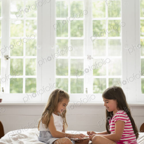 Two girls sitting and playing, using a digital tablet.