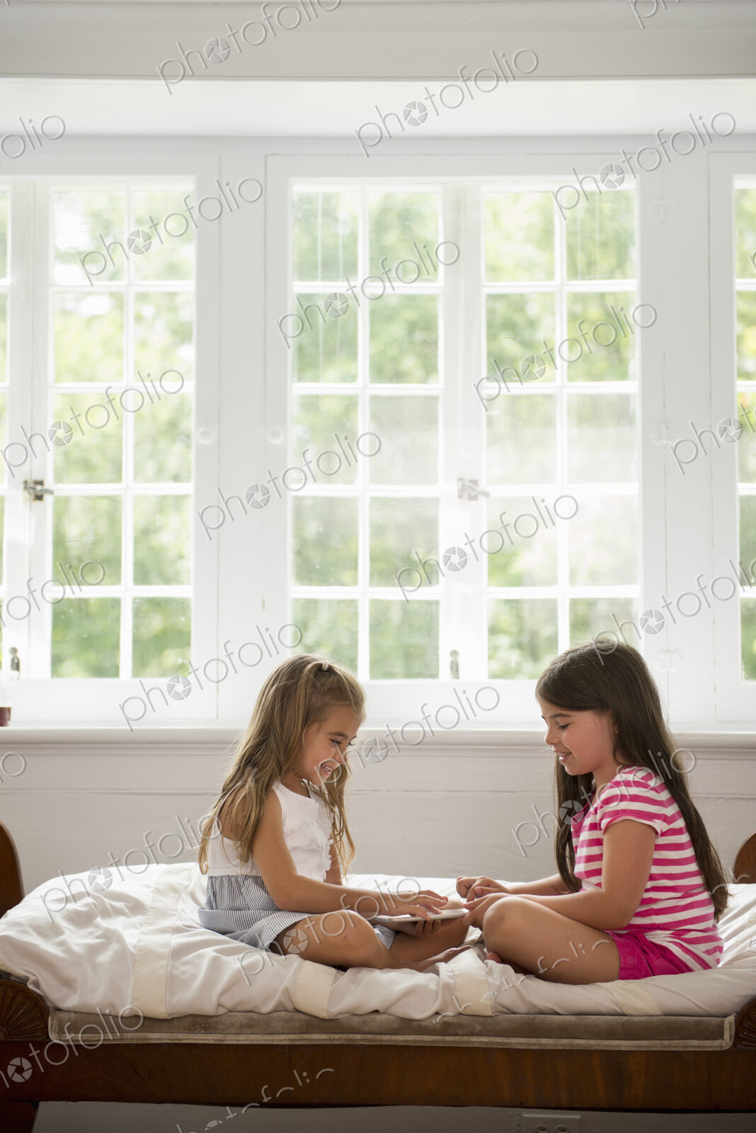 Two girls sitting and playing, using a digital tablet.