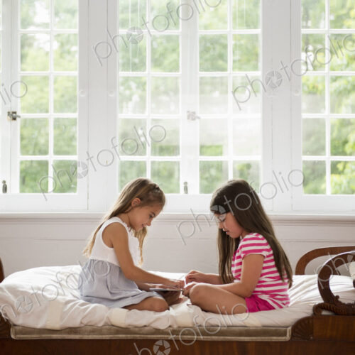 Two girls sitting and playing, using a digital tablet.