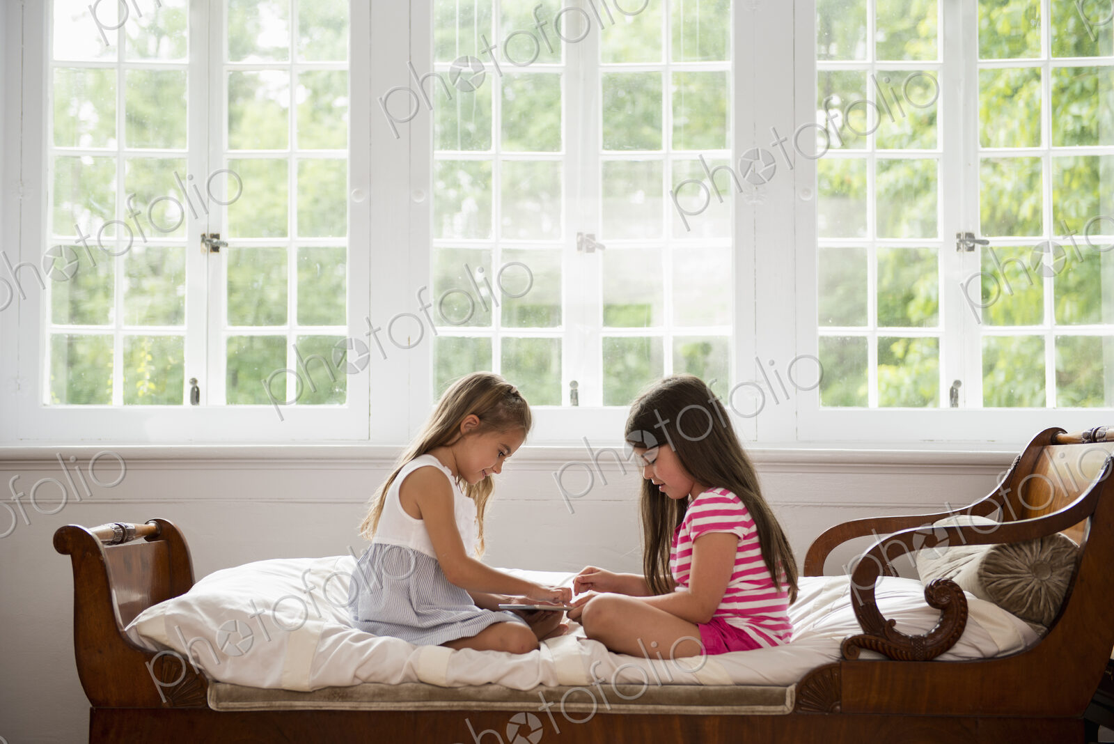 Two girls sitting and playing, using a digital tablet.