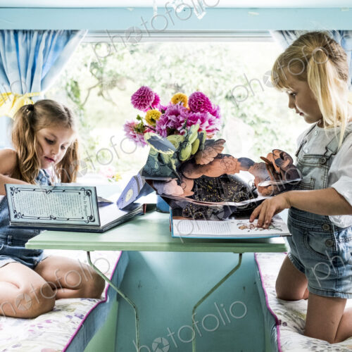 Two girls sitting at a table inside a blue caravan, playing. Two girls sitting at a table inside a blue caravan, playing.