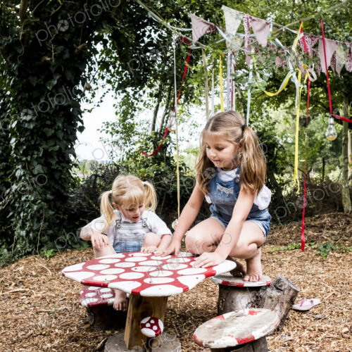 Two girls sitting at small wooden table in a garden, playing. Two girls sitting at small wooden table in a garden, playing.