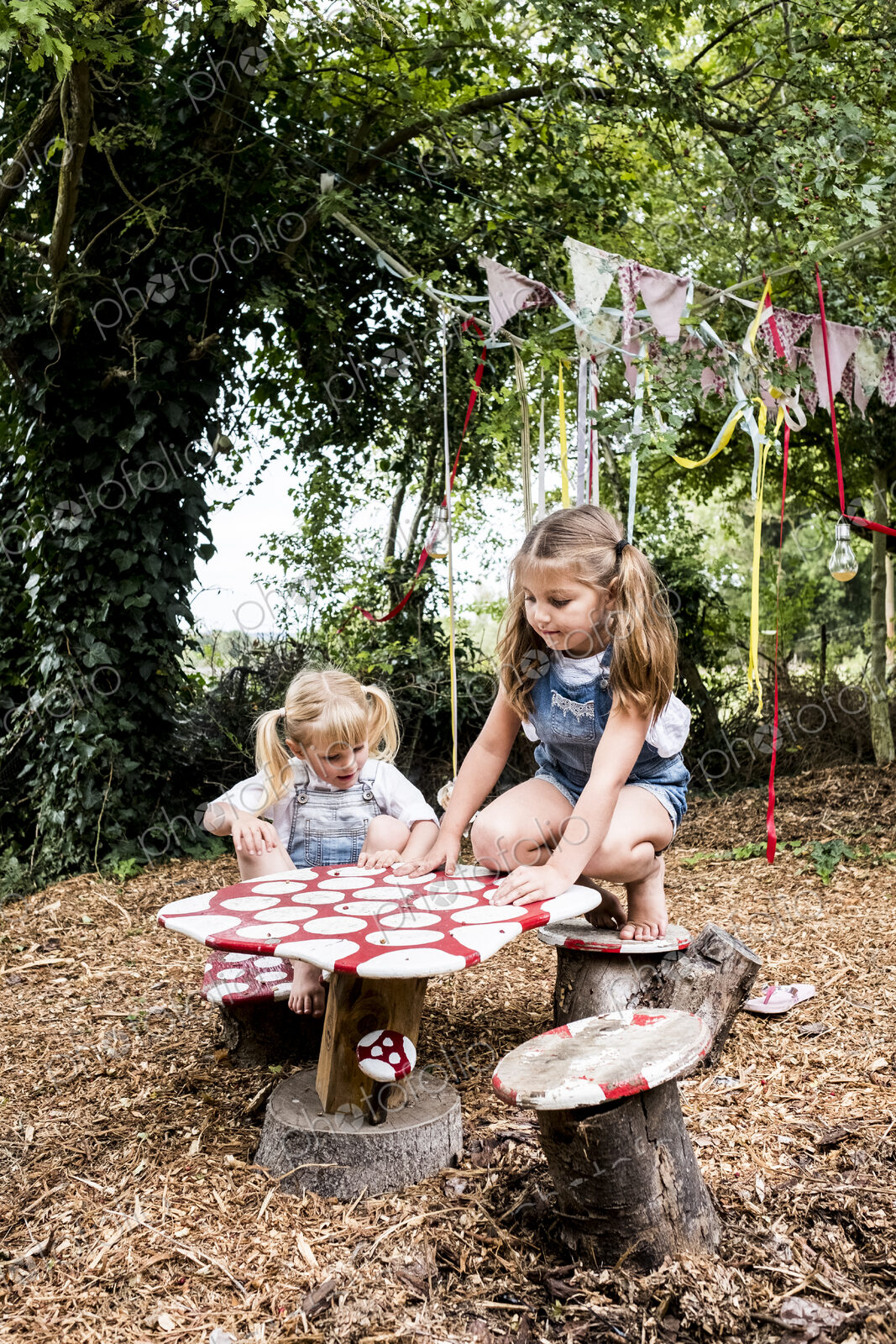 Two girls sitting at small wooden table in a garden, playing.