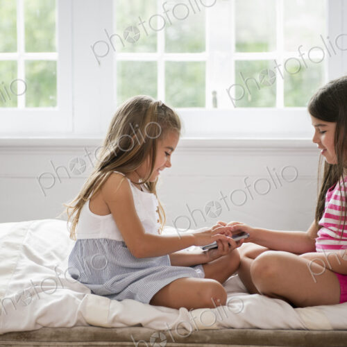 Two girls sitting cross legged facing each other, holding a smart phone.