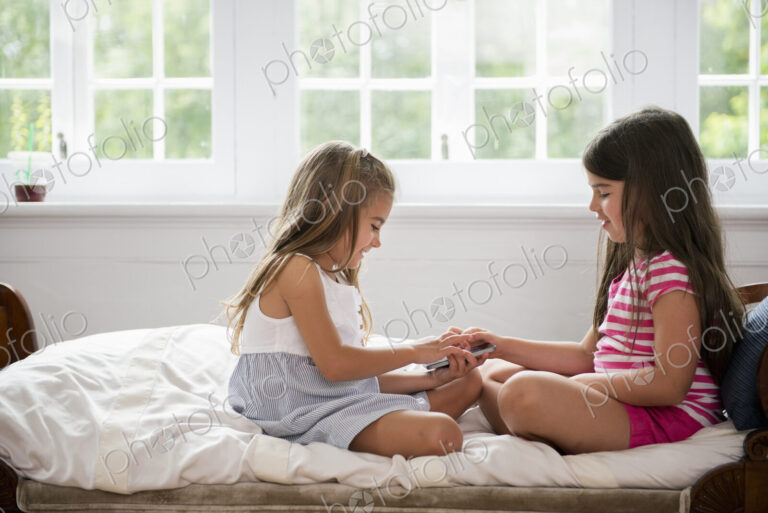 Two girls sitting cross legged facing each other, holding a smart phone.