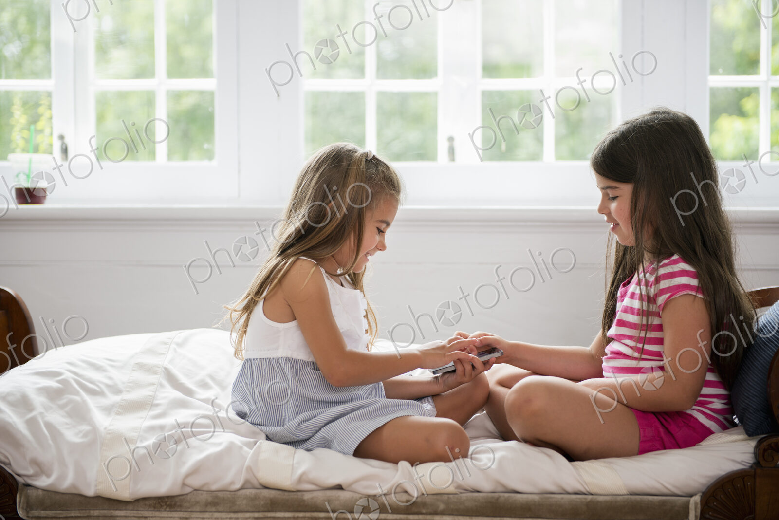 Two girls sitting cross legged facing each other, holding a smart phone.