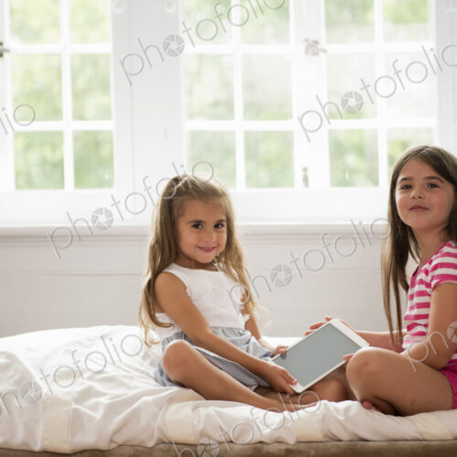 Two girls sitting holding a digital tablet.