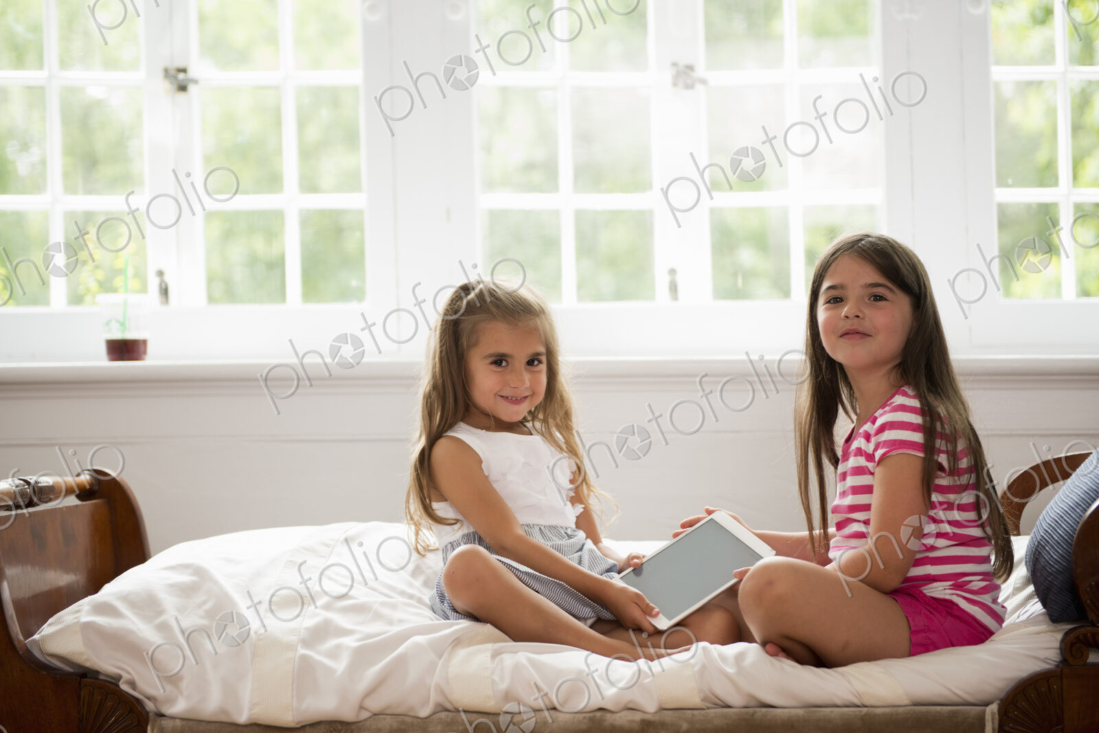 Two girls sitting holding a digital tablet.
