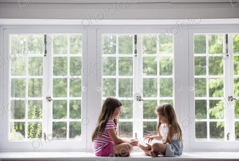 Two girls sitting indoors cross legged.