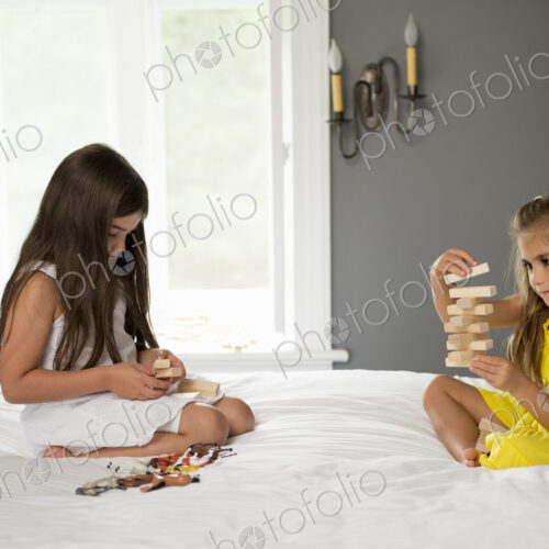 Two girls sitting on a bed playing together.
