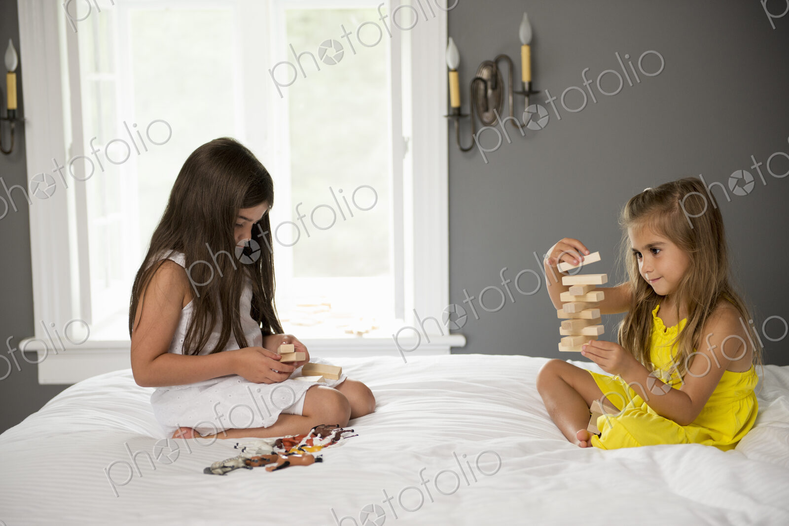 Two girls sitting on a bed playing together.