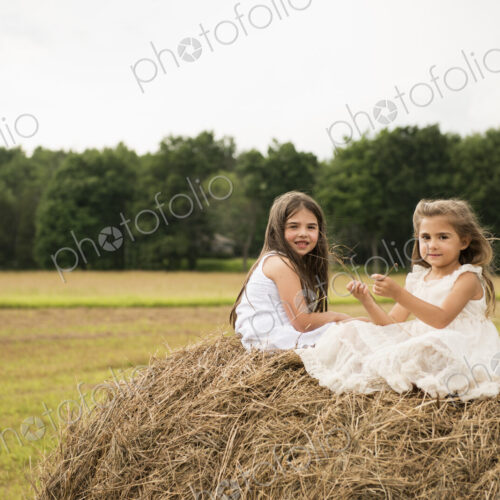Two girls sitting on top of a haystack playing. Two girls sitting on top of a haystack playing.