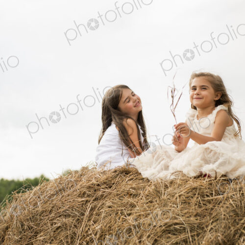 Two girls sitting on top of a haystack playing. Two girls sitting on top of a haystack playing.