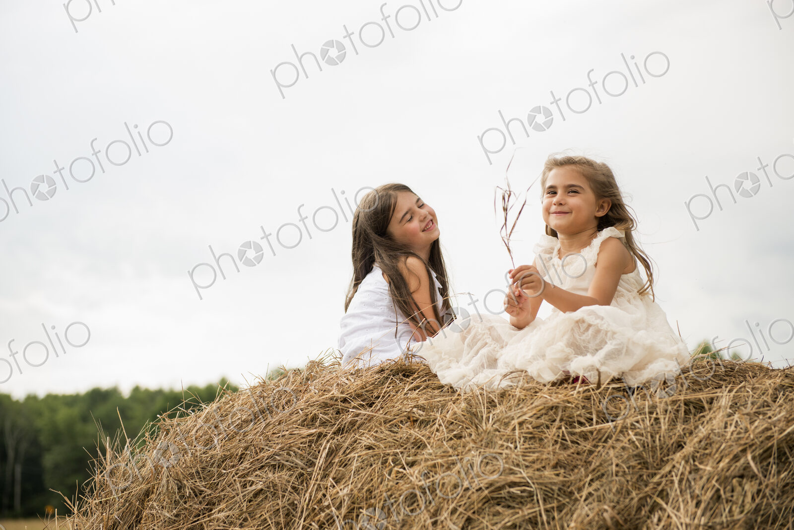 Two girls sitting on top of a haystack playing.