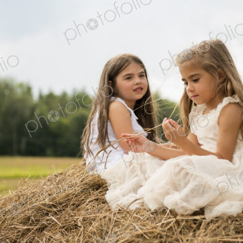 Two girls sitting on top of a haystack playing. Two girls sitting on top of a haystack playing.