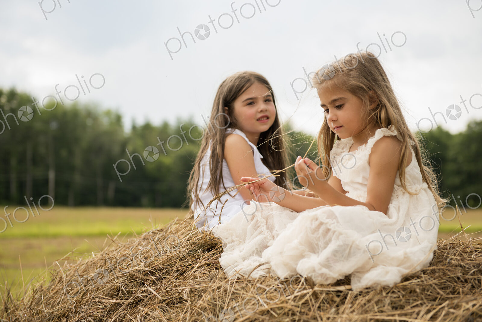 Two girls sitting on top of a haystack playing.