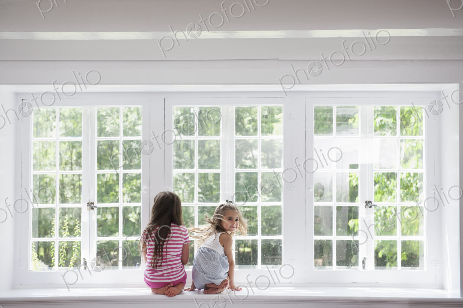 Two girls sitting side by side by a large window.