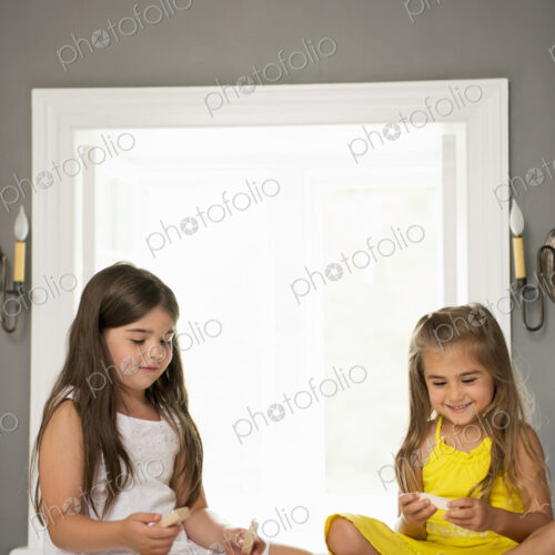 Two girls sitting together playing in a bedroom.