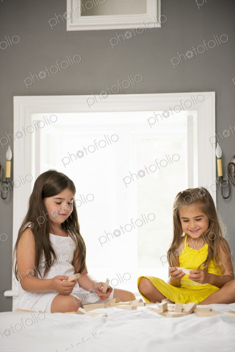 Two girls sitting together playing in a bedroom.