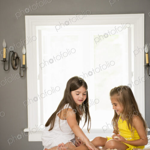 Two girls sitting together playing in a bedroom.