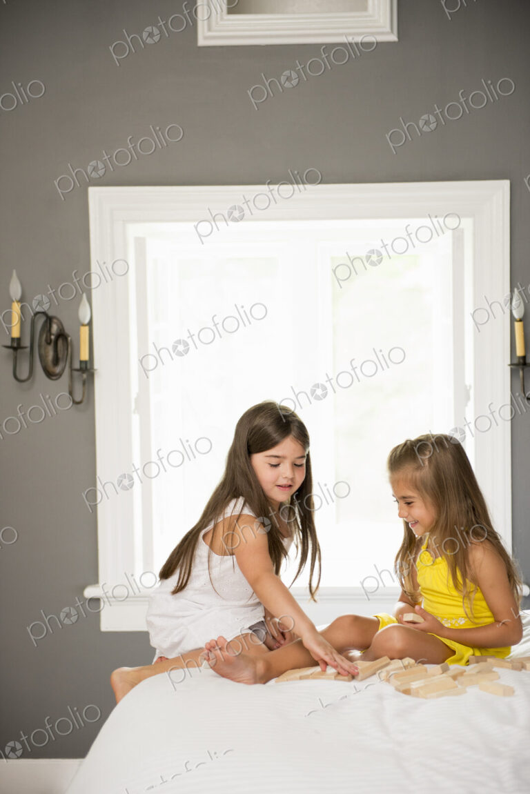 Two girls sitting together playing in a bedroom.
