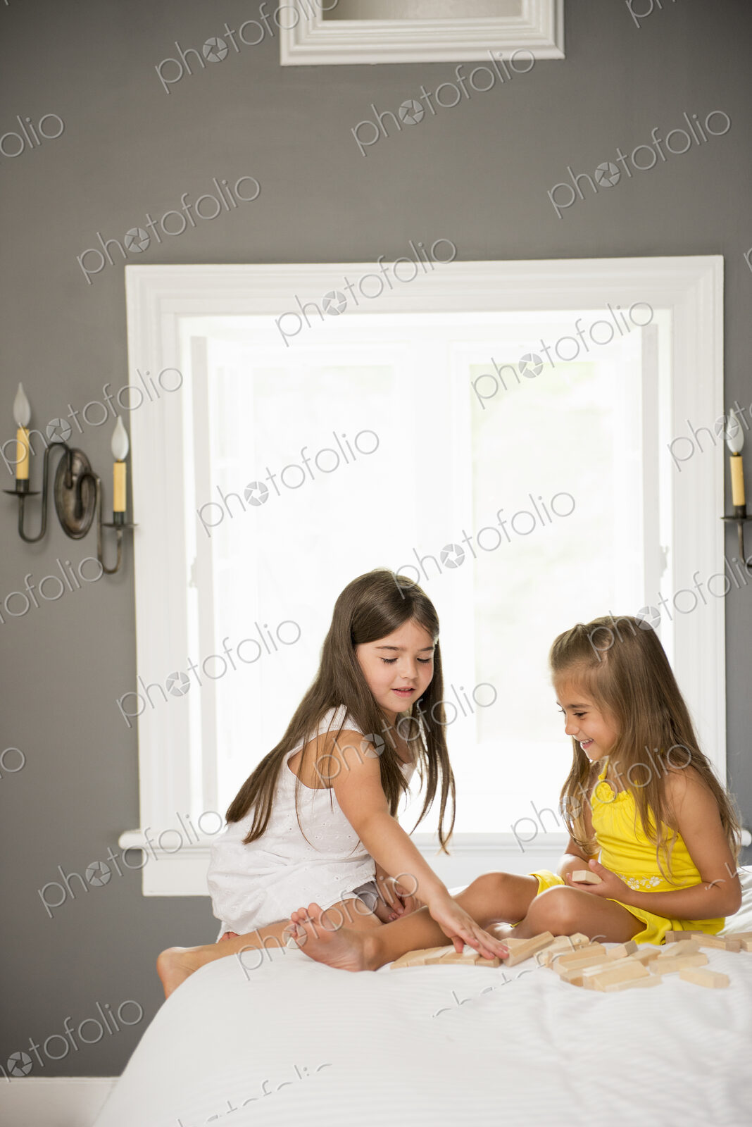Two girls sitting together playing in a bedroom.