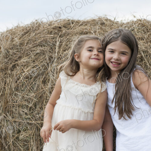 Two girls standing by a large haybale, smiling and sharing a secret. Two girls standing by a large haybale, smiling and sharing a secret.
