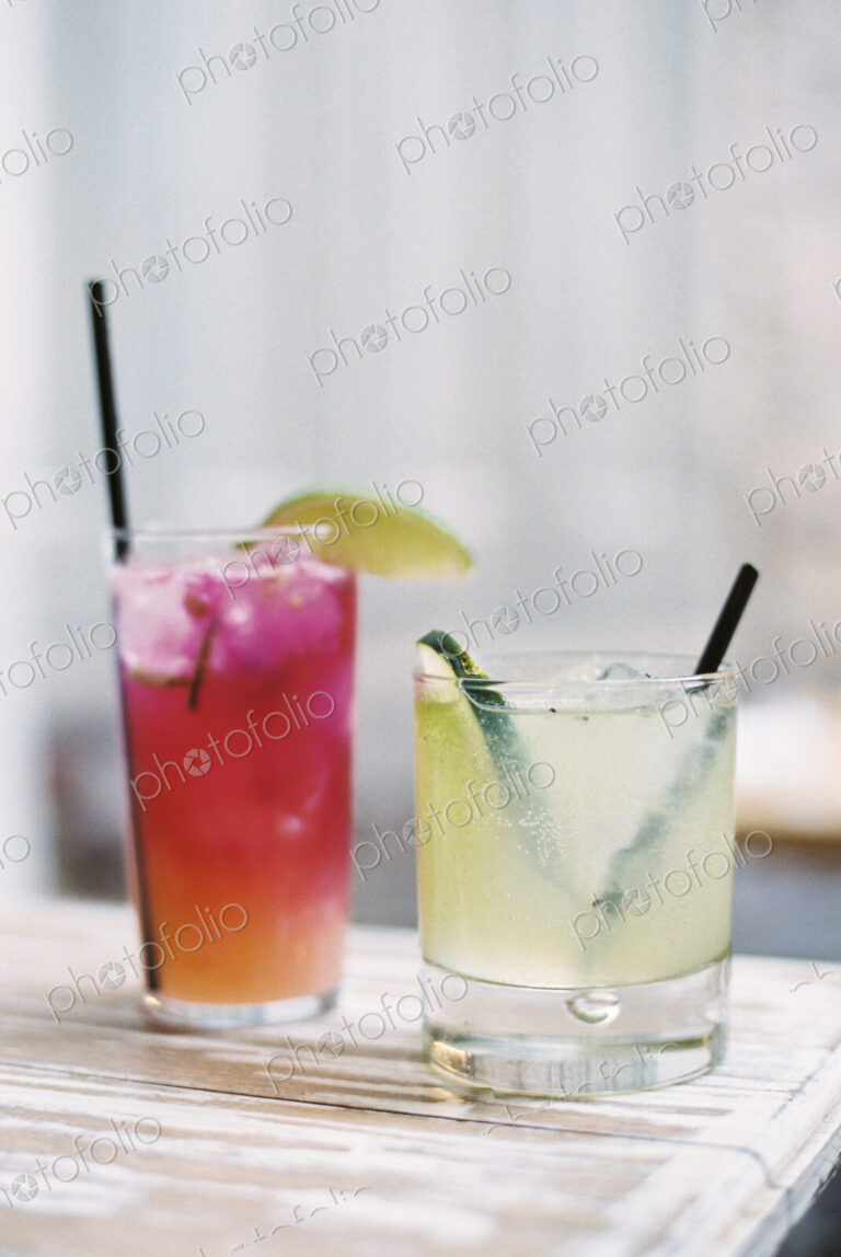 Two glasses of chilled drinks, with straws and garnishes. Lemonade and iced tea.