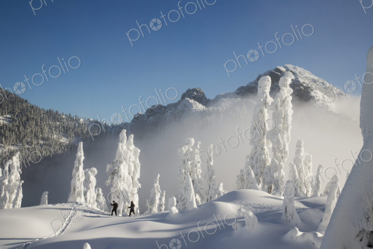 Two hikers enjoy a blue bird day in the middle of winter in the snow covered Cascade…