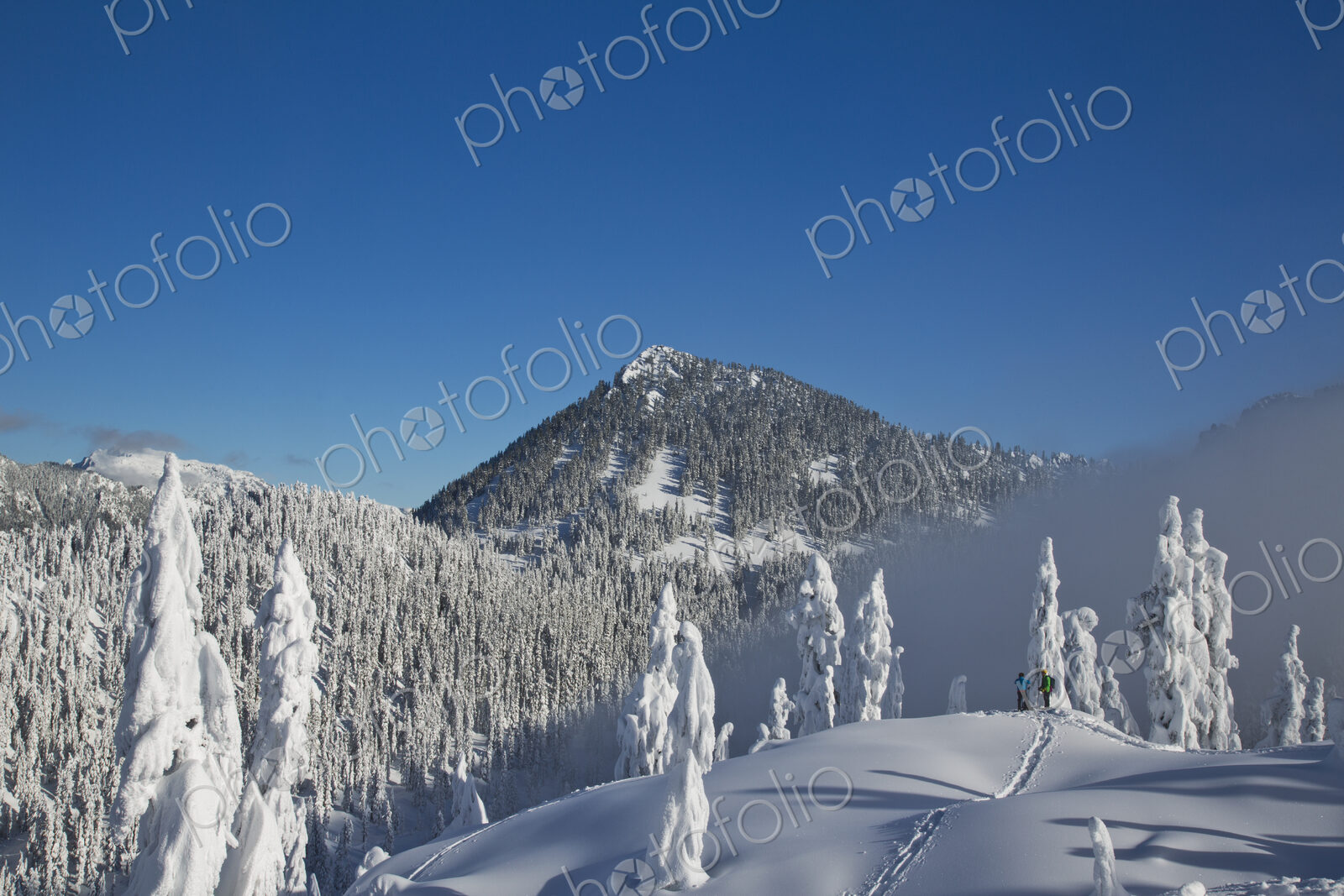 Two hikers enjoy a blue bird day in the middle of winter in the snow covered Cascade…