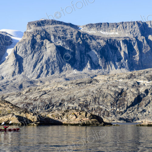 Two kayakers on the water off the rocky shore, Greenland.