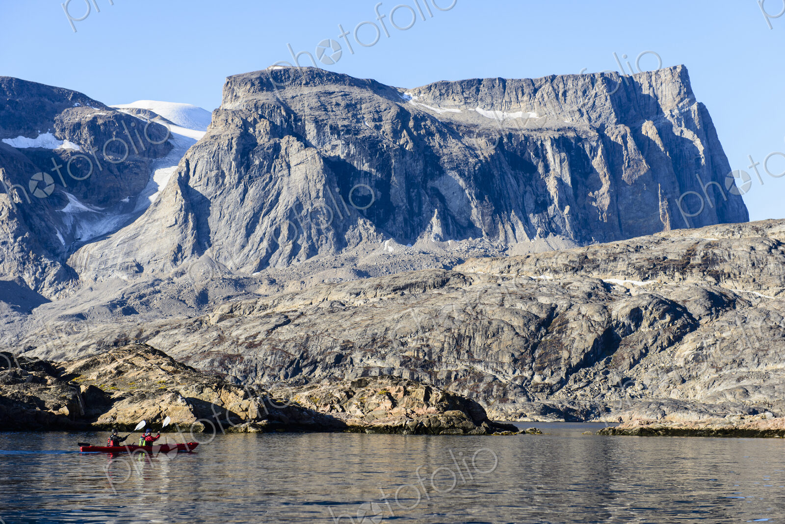 Two kayakers on the water off the rocky shore, Greenland.