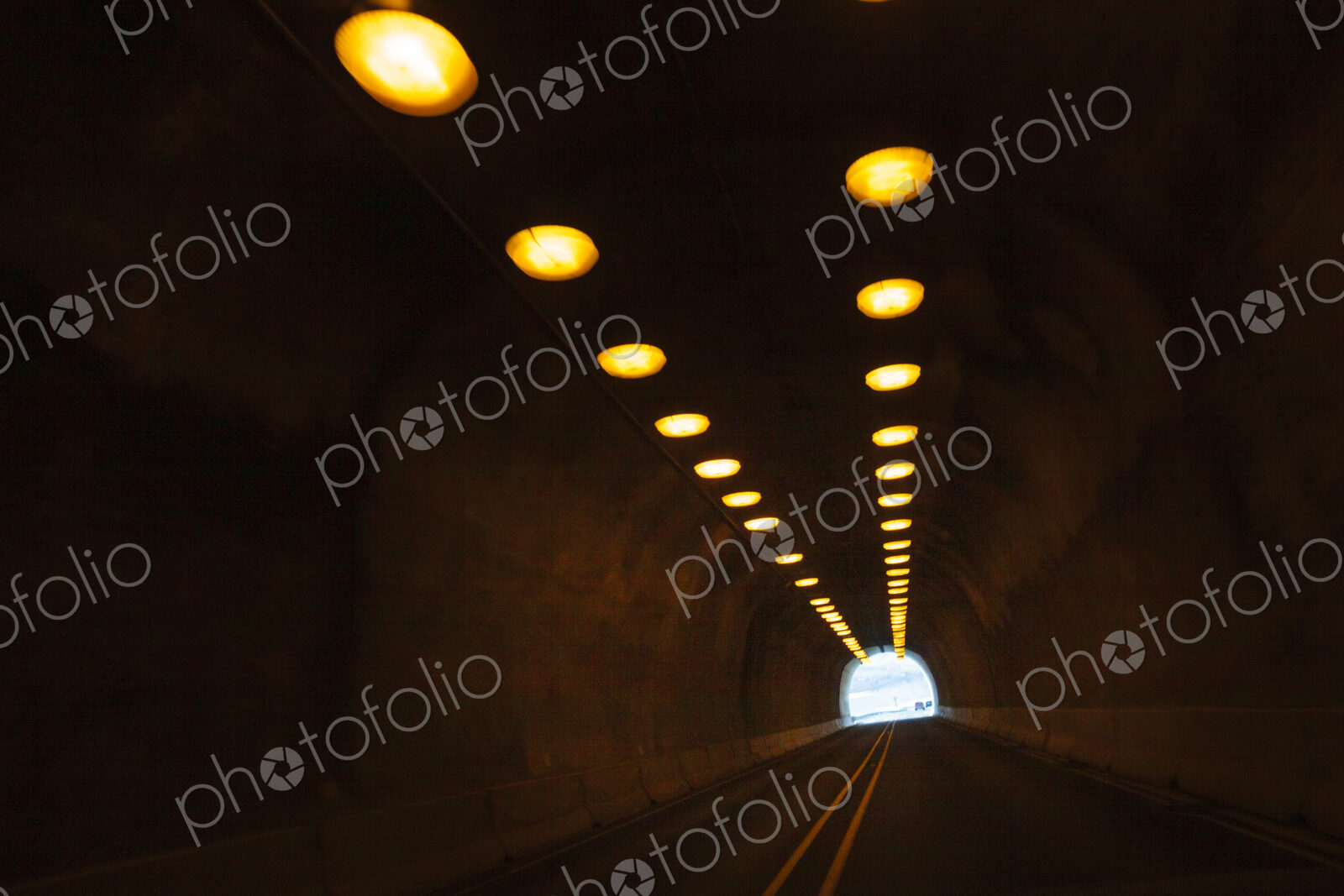 Two lane highway through a tunnel, view of the lights leading to the daylight and the…