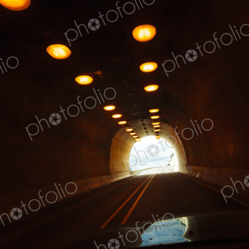 Two lane highway through a tunnel, view of the lights leading to the daylight and the…