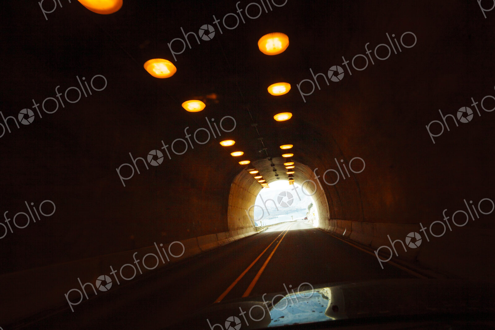 Two lane highway through a tunnel, view of the lights leading to the daylight and the…