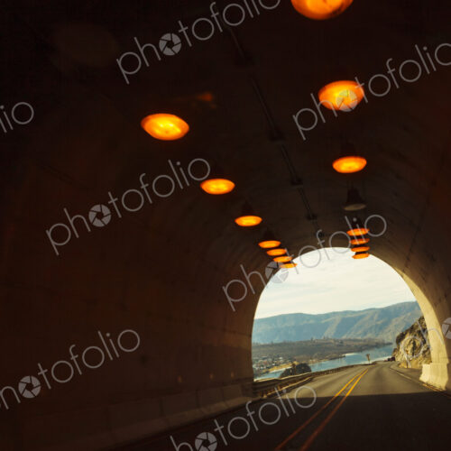 Two lane highway through a tunnel, view of the lights leading to the daylight and the…