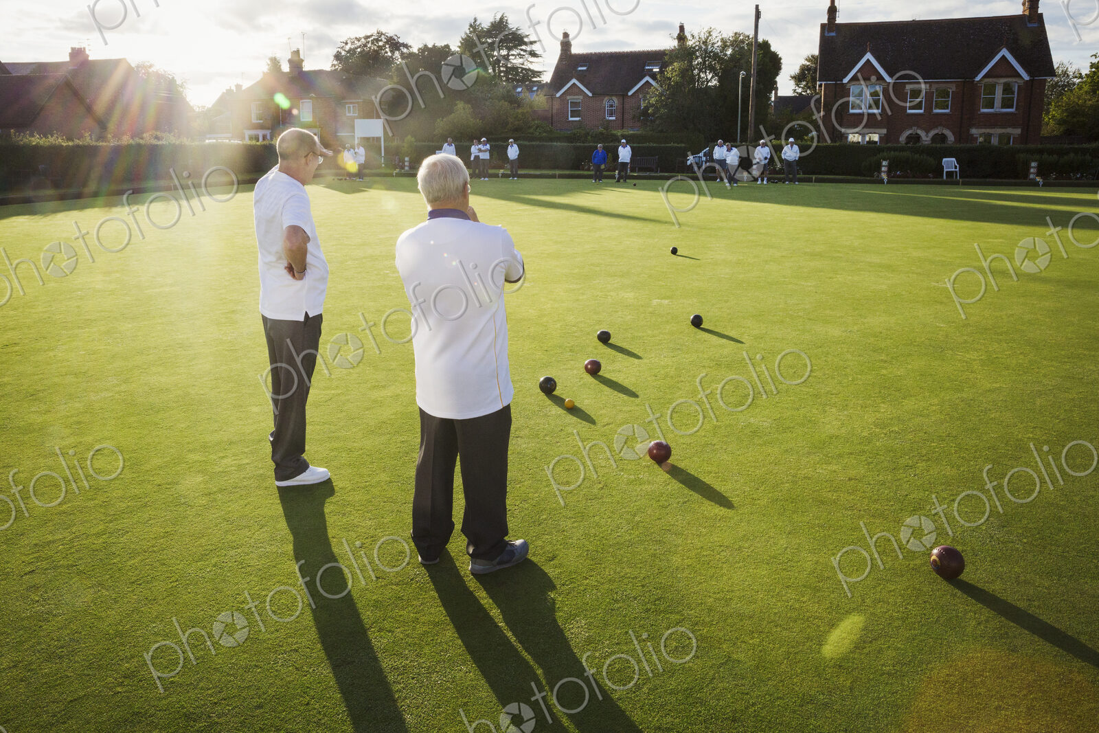 Two lawn bowls players, men standing discussing the game, and a clutch of lawn bowls…