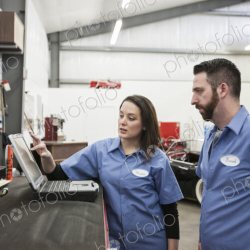 Two mechanics working on a laptop computer in a repair shop.