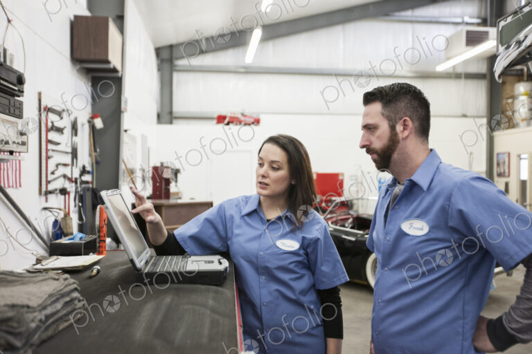Two mechanics working on a laptop computer in a repair shop.