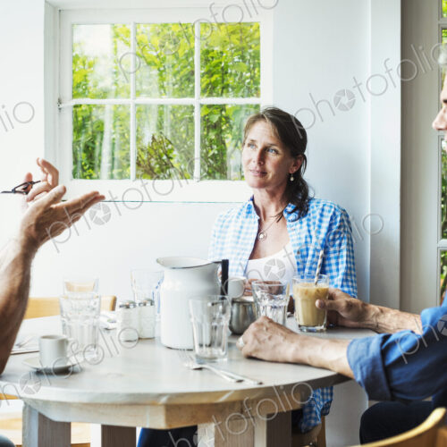 Two men and a woman seated at a coffee shop table talking.