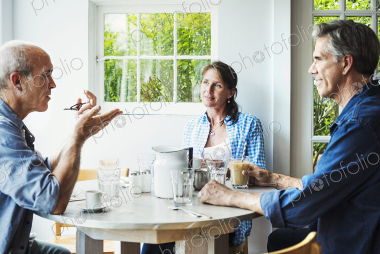 Two men and a woman seated at a coffee shop table talking.