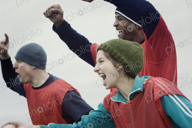 Two men and one woman, friends cheering on their team at a winter sporting event.
