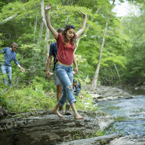 Two men and two women on the riverbank, one leaping across stepping stones. Two men and two women on the riverbank, one leaping across stepping stones.