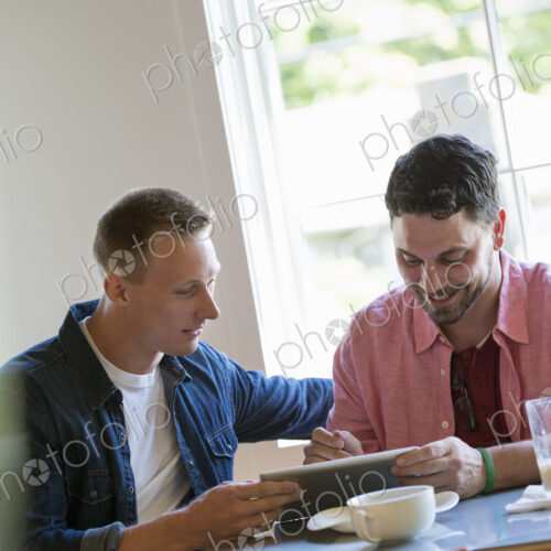 Two men at a cafe table, using a digital tablet. Two men at a cafe table, using a digital tablet.