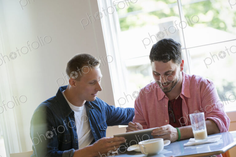 Two men at a cafe table, using a digital tablet.