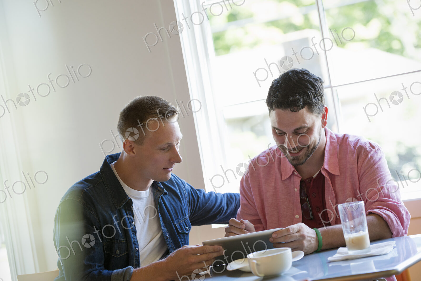 Two men at a cafe table, using a digital tablet.